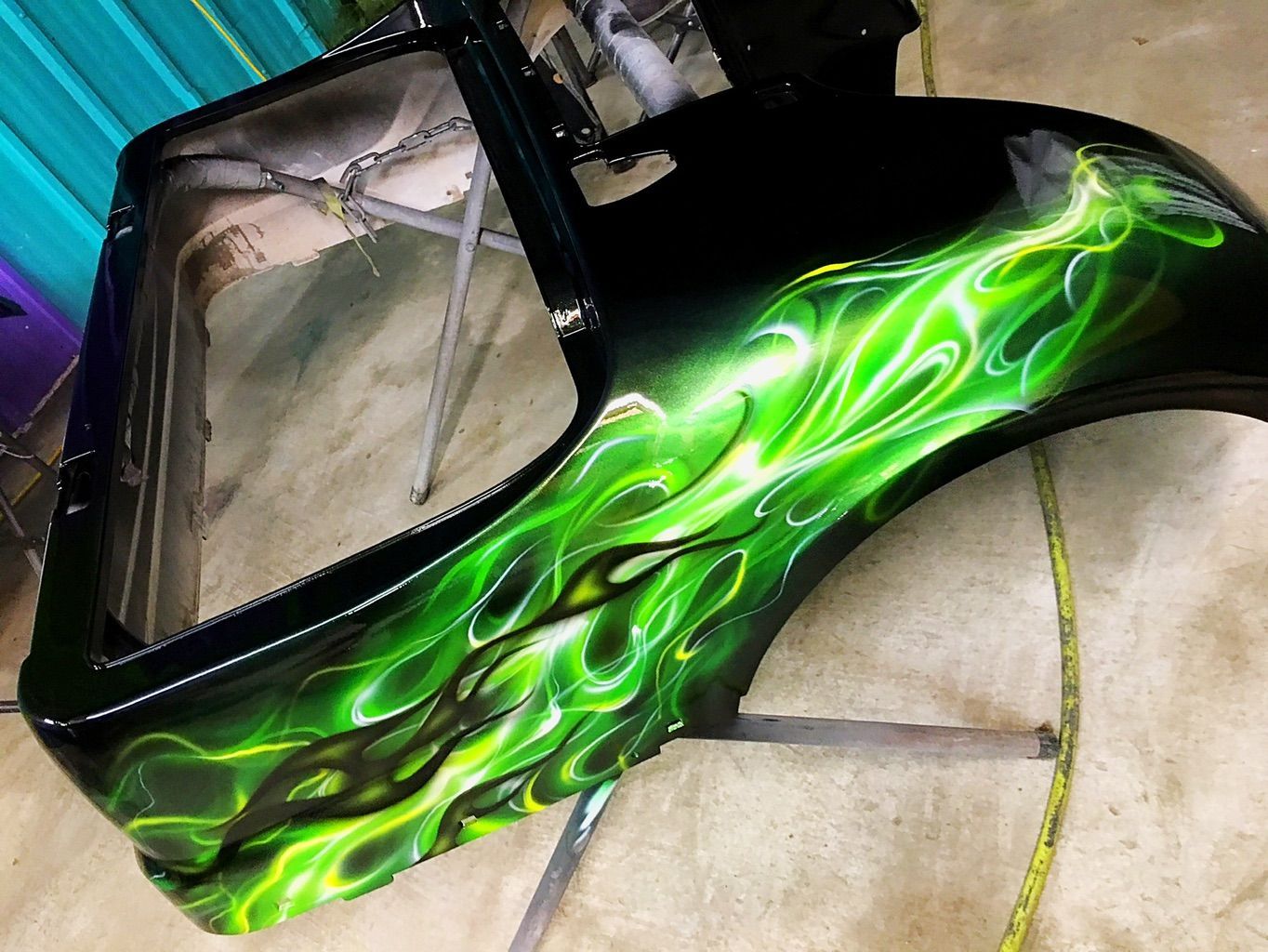 A glossy black body panel airbrushed with layered, glowing lime-green flames.