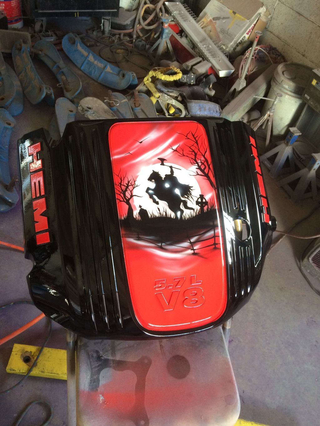 A black and red engine cover airbrushed with a headless horseman galloping past bare trees and a graveyard under a red sky.