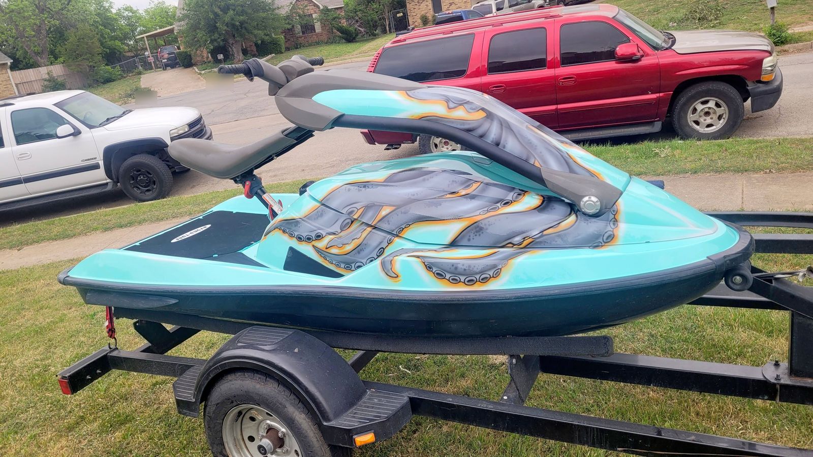 A teal jet ski on its trailer with grey octopus tentacles, outlined in orange, airbrushed across the deck behind the seat.