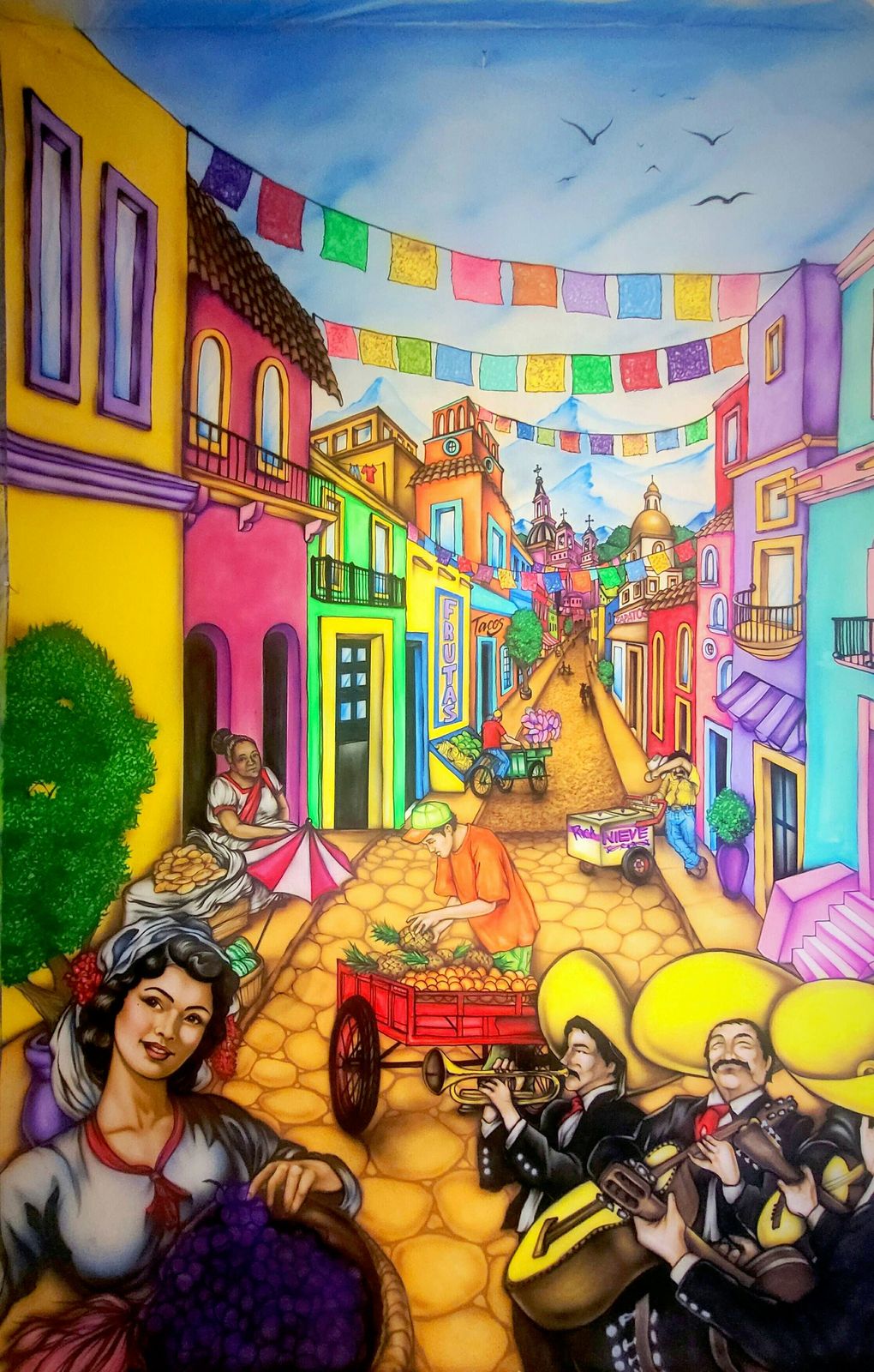 A tall mural of a colourful Mexican street lined with pink, yellow and purple houses under strings of papel picado, with a woman holding a basket of grapes and mariachi musicians in the foreground.