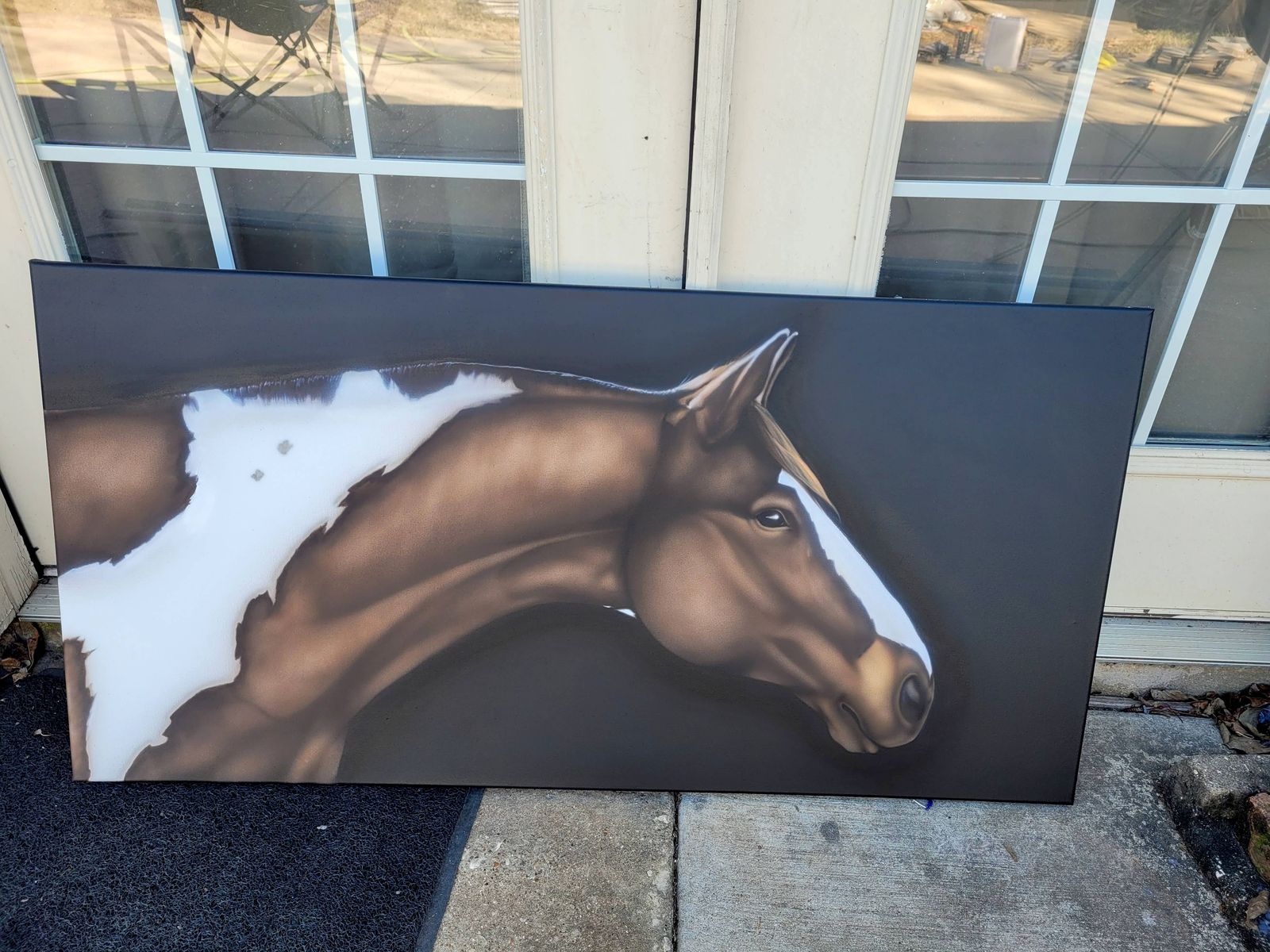 A wide airbrushed panel of a brown and white paint horse's head and neck on a black background, leaning against a door.