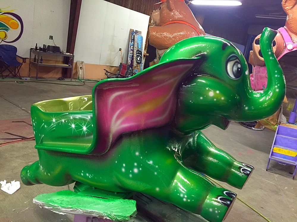 A fibreglass elephant ride seat in a workshop, painted glossy green with sparkles and pink-shaded ears.