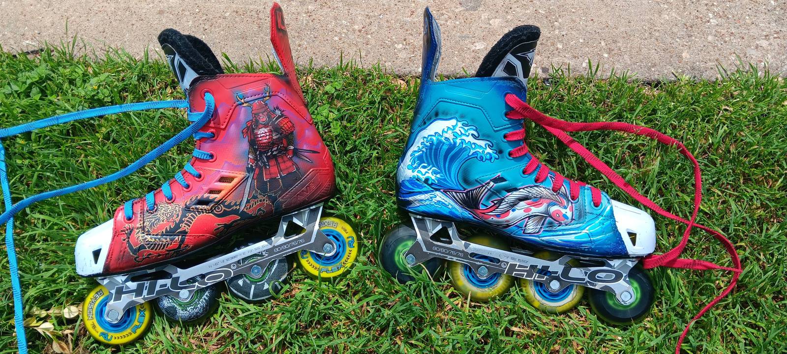 Two inline skates on grass, one boot painted red with a warrior figure, the other blue with a breaking wave.